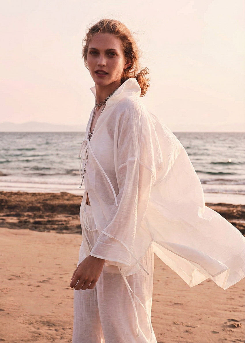 Woman in a white outfit standing on a beach with ocean in the background