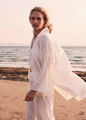 Woman in a white outfit standing on a beach with ocean in the background