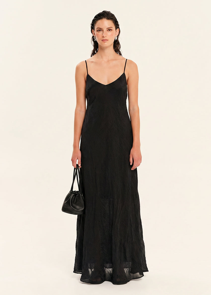 Woman wearing a black slip dress holding a black handbag on a beige background