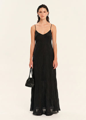 Woman wearing a black slip dress holding a black handbag on a beige background