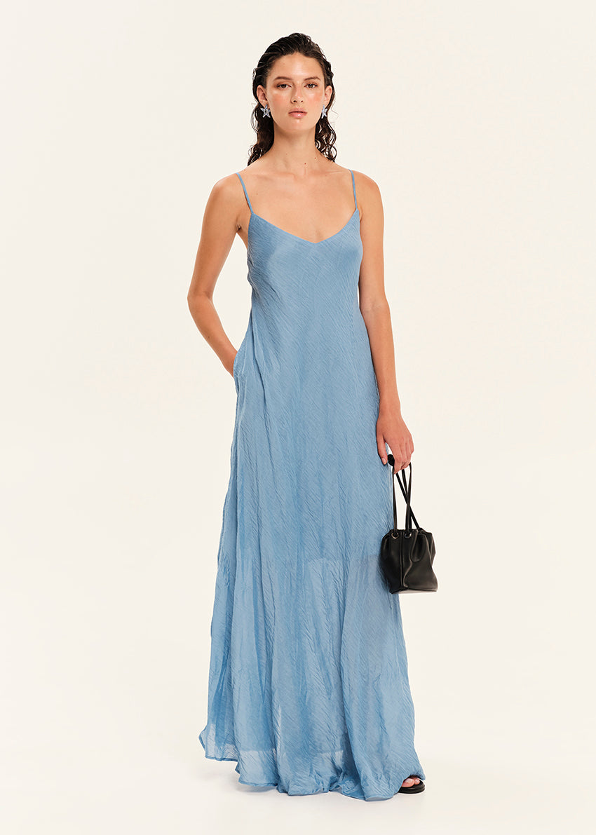 Woman wearing a blue slip dress holding a black handbag on a white background