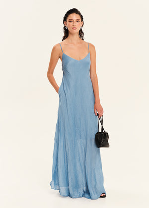 Woman wearing a blue slip dress holding a black handbag on a white background