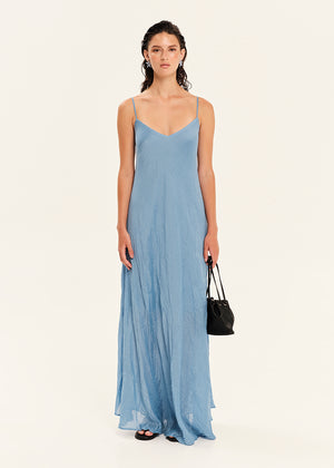 Woman wearing a long light blue dress holding a black handbag on a white background
