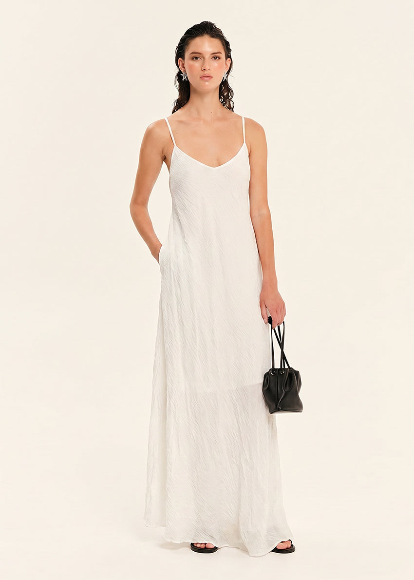 Woman wearing a white slip dress holding a black handbag on a beige background