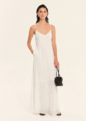Woman wearing a white slip dress holding a black handbag on a beige background
