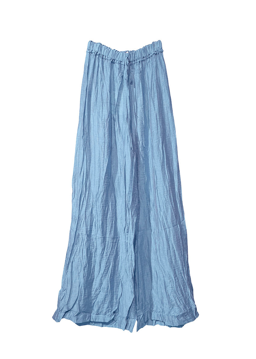 Woman in a light blue shirt with matching pants standing on a beach with ocean in the background