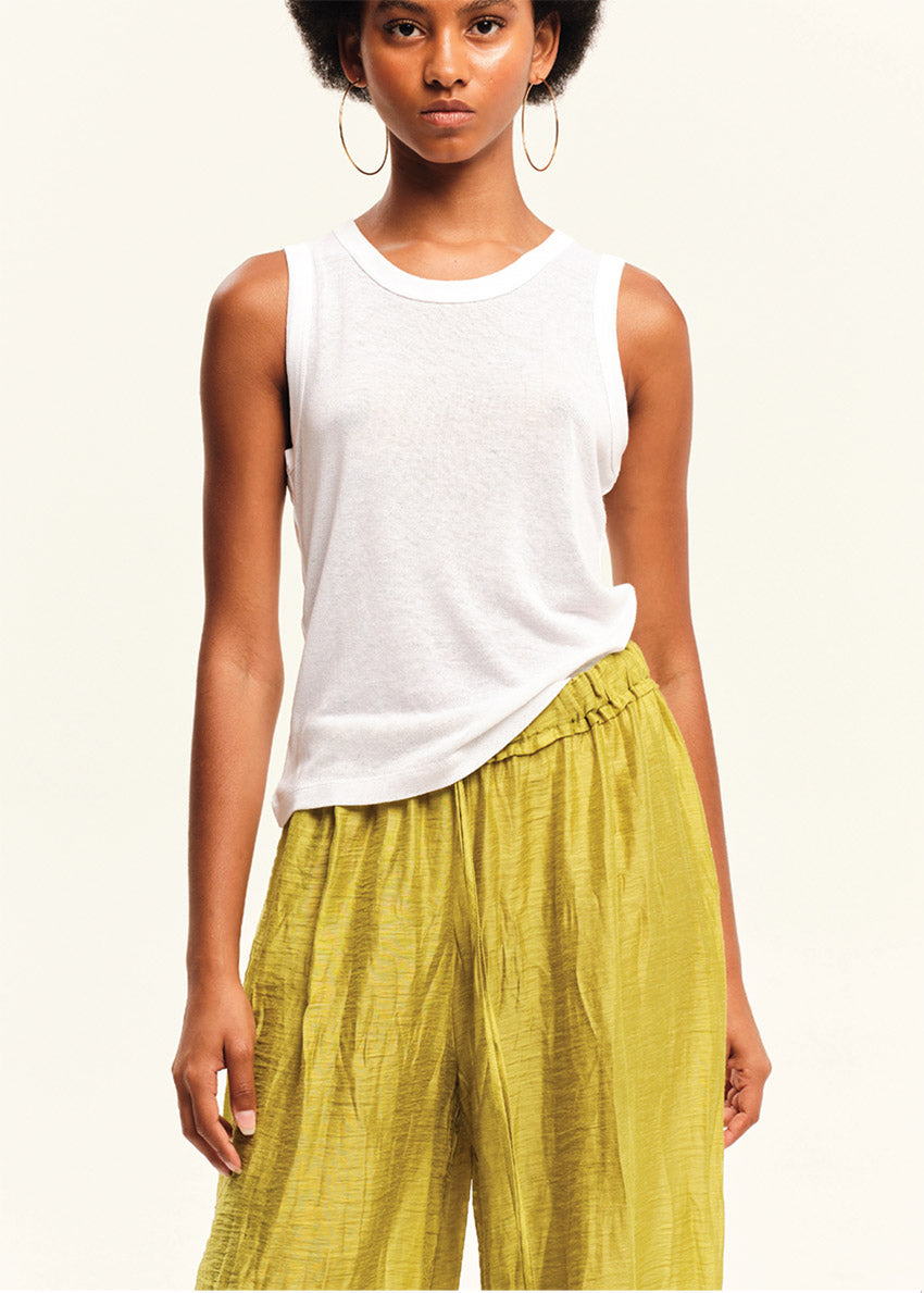 Woman wearing a white sleeveless top and green pants on a plain background
