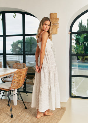 Woman in a white dress standing in a modern indoor setting with large windows.