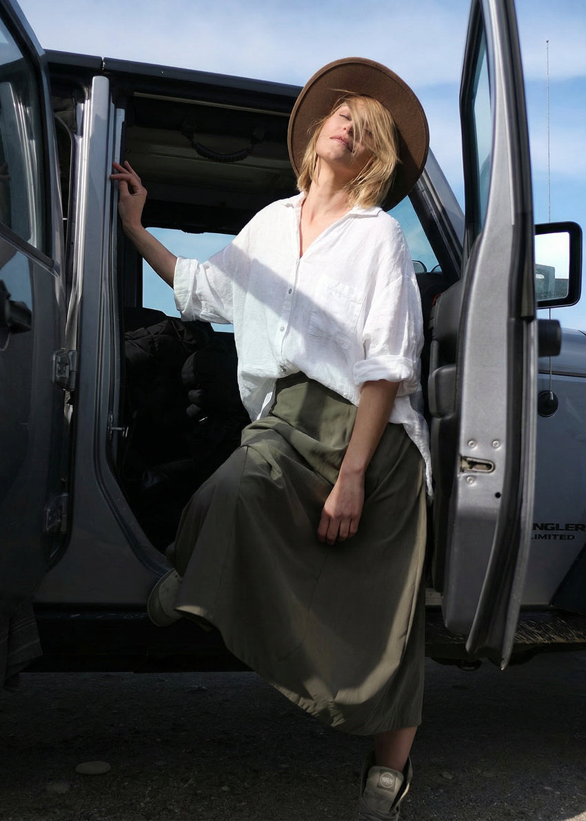 Woman in a white shirt and green skirt standing next to an open car door with a blue sky background