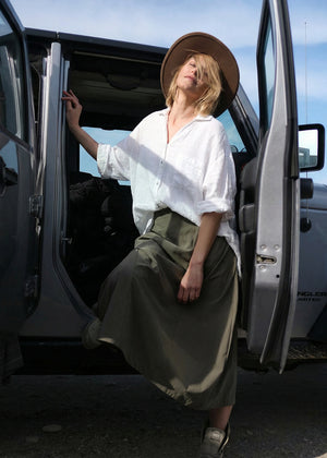 Woman in a white shirt and green skirt standing next to an open car door with a blue sky background
