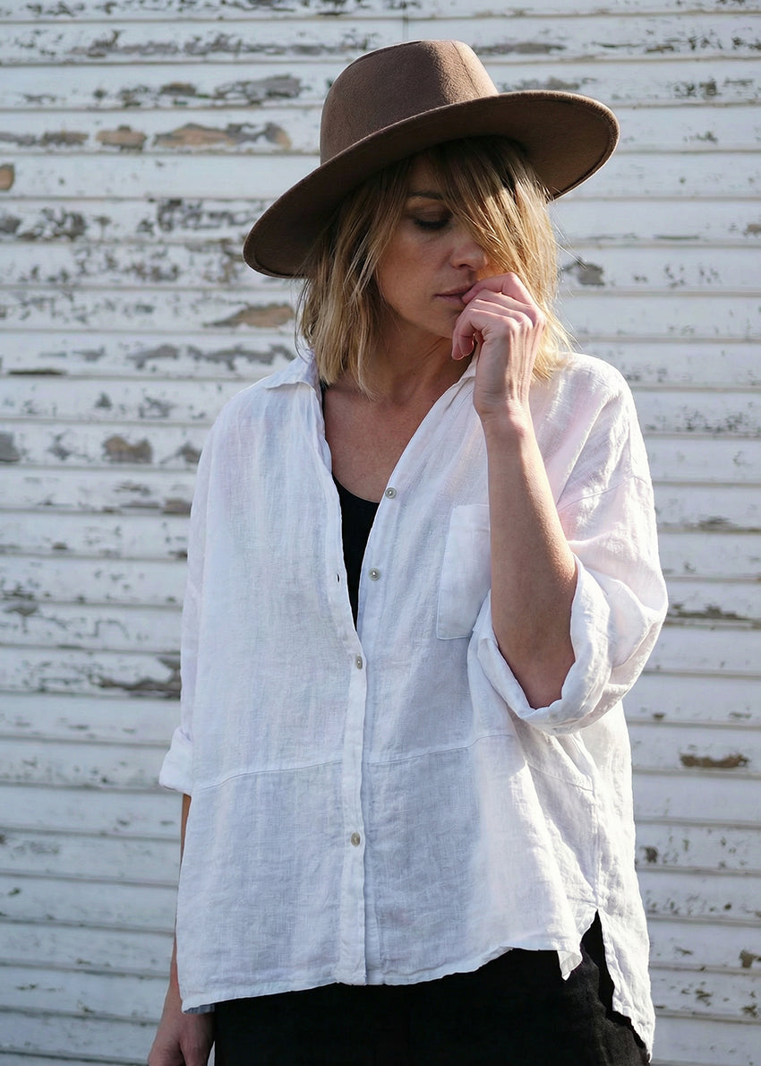 Woman wearing a white shirt and brown hat against a rustic wall.