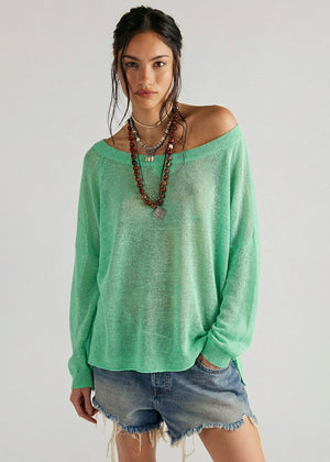 Woman wearing a green sweater and denim shorts against a plain background