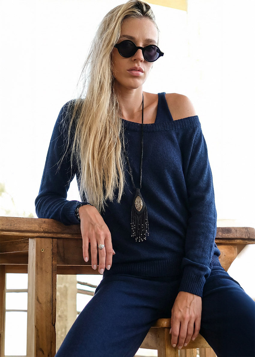 Woman wearing a blue off-shoulder sweater and sunglasses, sitting on a wooden bench.