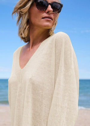 Woman in a beige cover-up on a beach with sunglasses