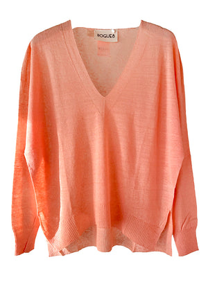 A pink Aie Salmon Sweater with a deep V-neck, dropped sleeves, and slits on the sides, displayed on a white background.