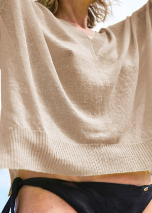 Close-up of a tan linen sweater with a deep V-neck and long over the wrist sleeves, showing the texture and drape of the fabric.