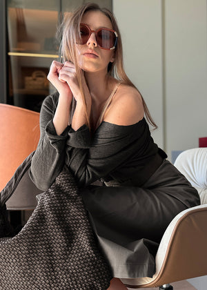 Woman wearing sunglasses and a dark outfit sitting on a chair.