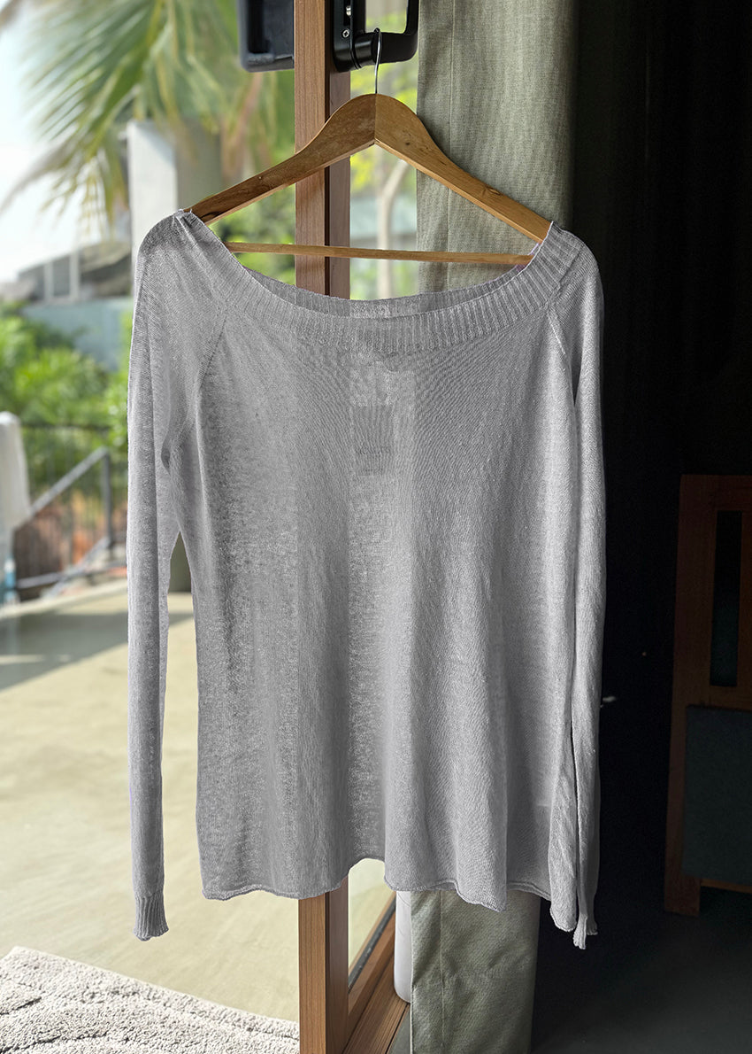 A light gray sweater hanging on a wooden hanger, displayed in a home environment.