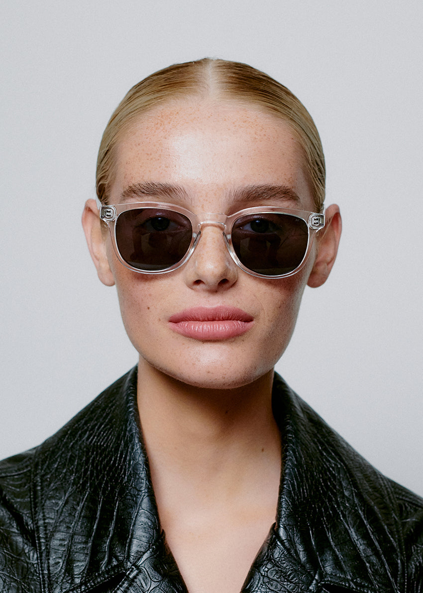 Woman wearing dark sunglasses and a black leather jacket against a light gray background