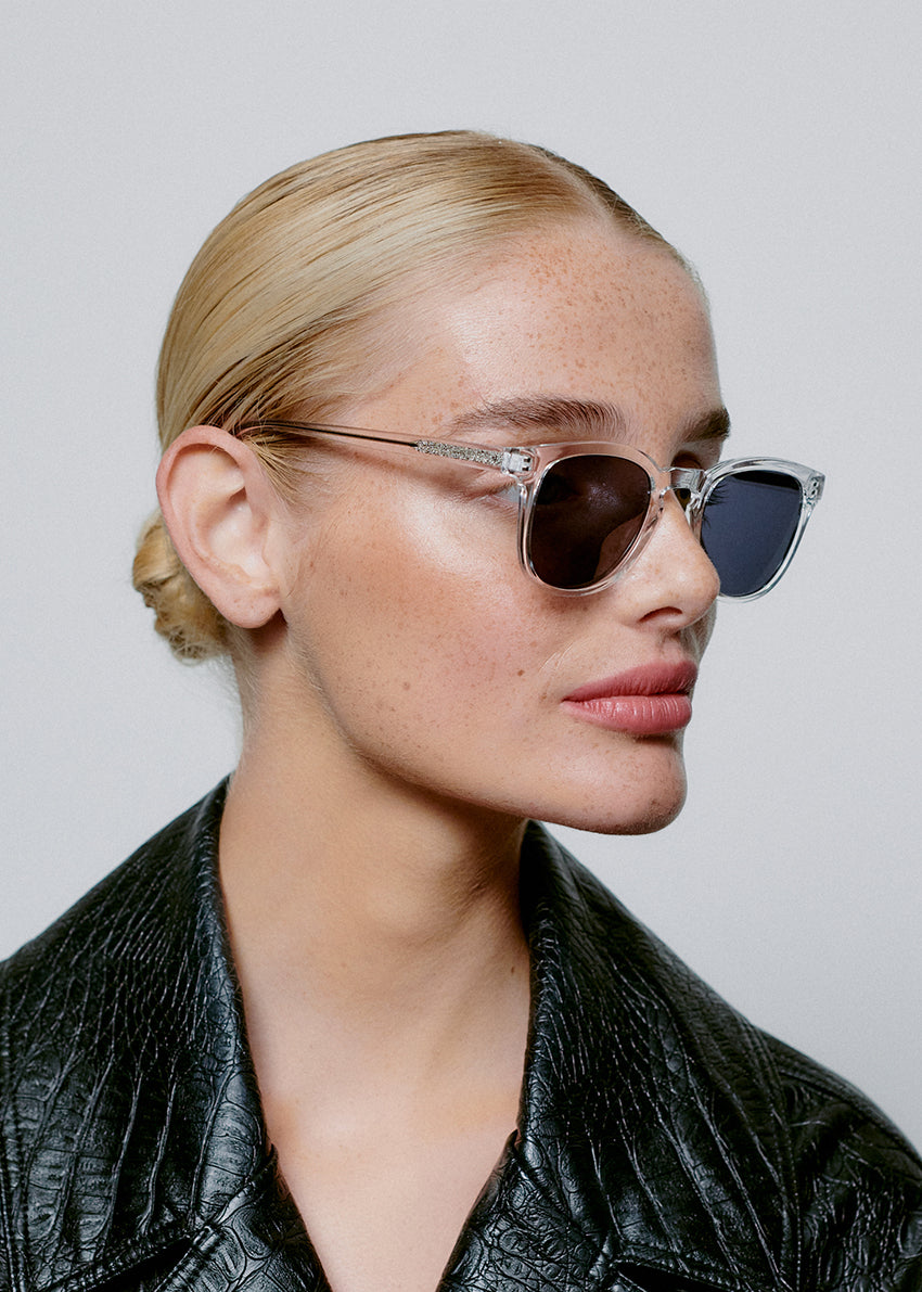 Person wearing sunglasses and a black leather jacket against a plain background