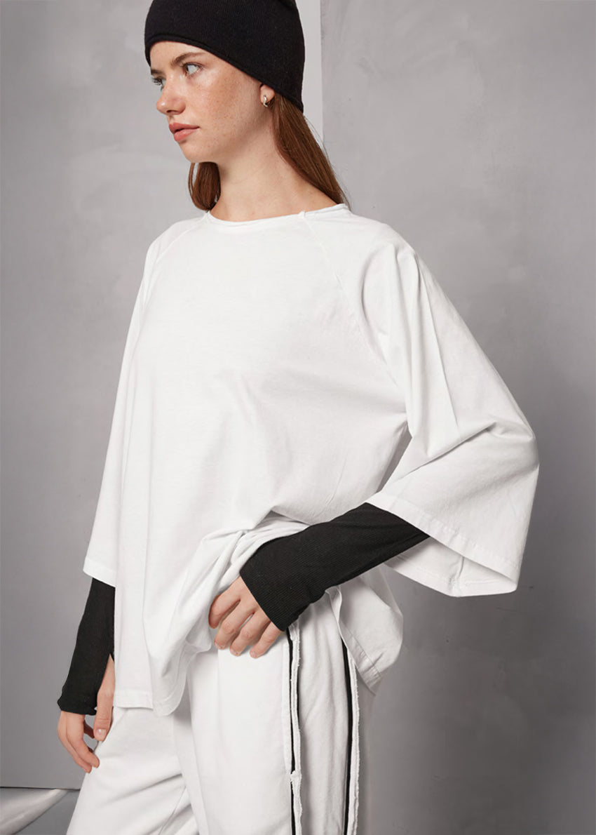 Person wearing a white oversized shirt with black sleeves and a black beanie against a gray background