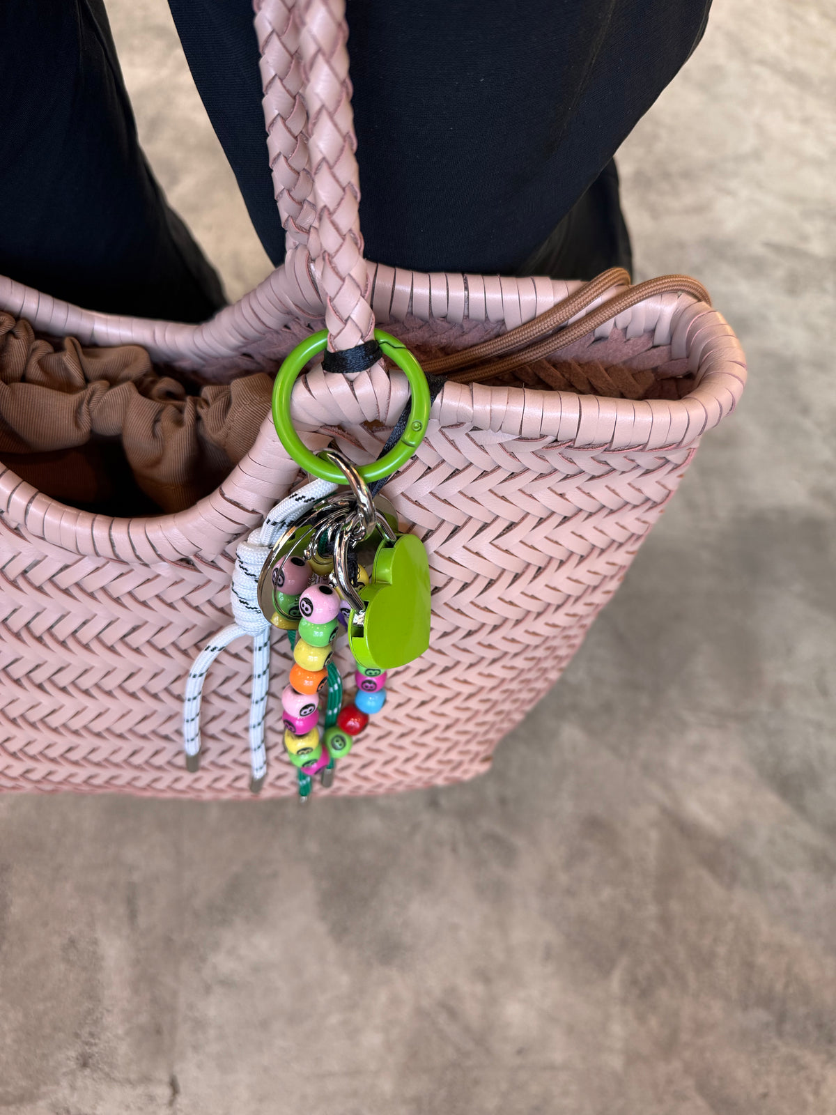 Pink woven handbag with colorful keychain and green tag on a neutral background