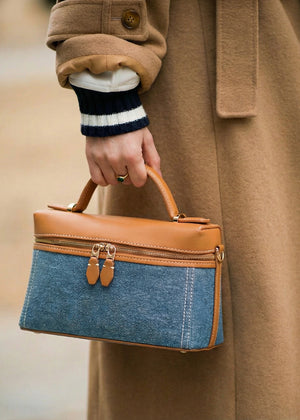 Person holding a blue and brown handbag with a beige coat