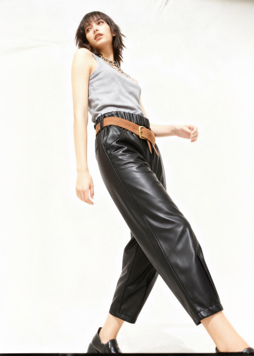 Person wearing a gray sleeveless top and black leather pants with a brown belt on a white background