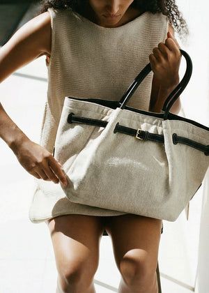Person holding a beige tote bag with black handles indoors