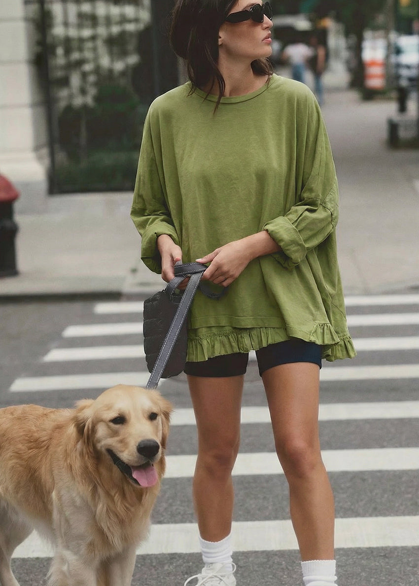 Woman in green sweater and shorts walking a dog on a city street.