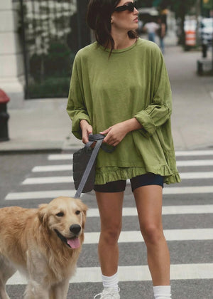 Woman in green sweater and shorts walking a dog on a city street.