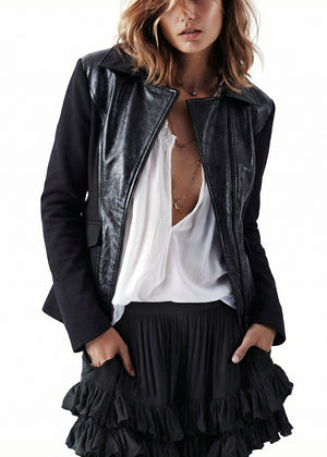Person wearing a black leather jacket over a white top and black ruffled skirt on a white background