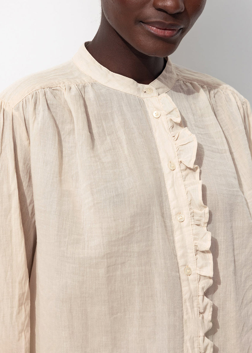 Close-up of a beige shirt with ruffles and buttons on a plain background