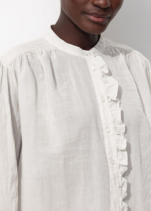 White blouse with ruffled details worn by a person against a neutral background