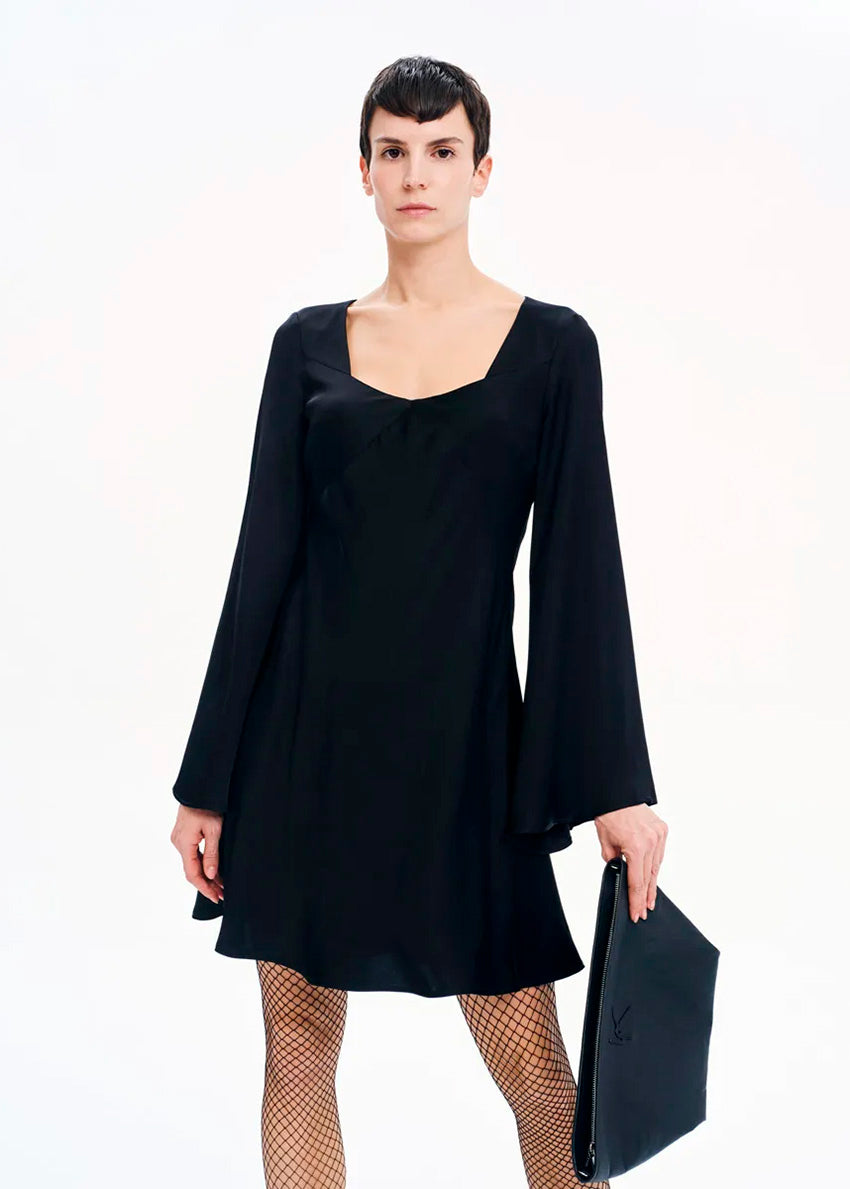 A model wearing a black mini dress with long bell sleeves and a V-neckline, standing against a white background.