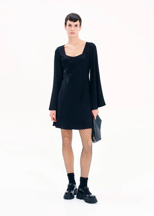 A model wearing a black mini dress with long bell sleeves and a V-neckline, standing against a white background.
