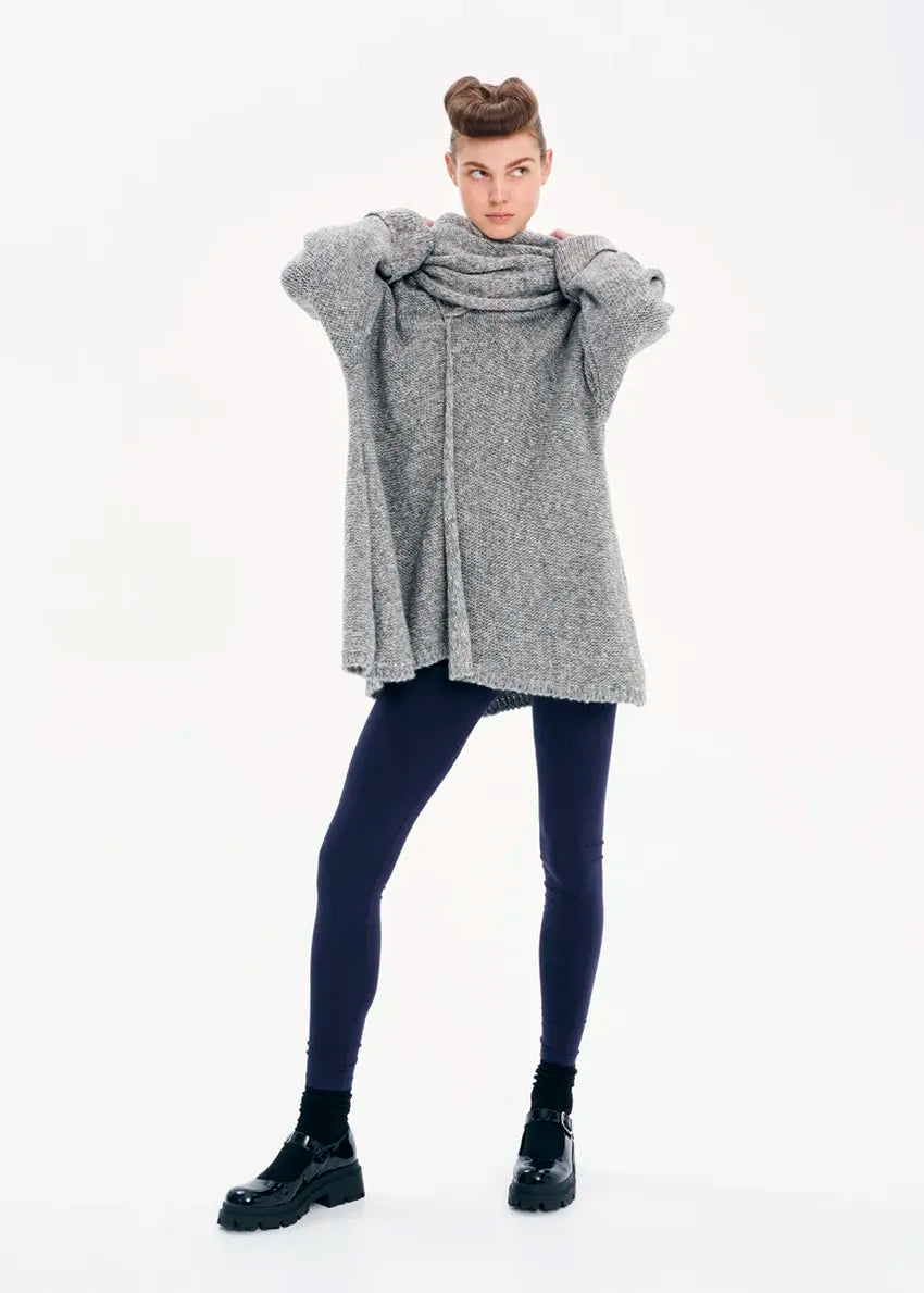 A model wearing a gray knit cardigan with long sleeves and a non-detachable scarf, paired with dark pants and black boots.