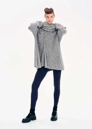 A model wearing a gray knit cardigan with long sleeves and a non-detachable scarf, paired with dark pants and black boots.