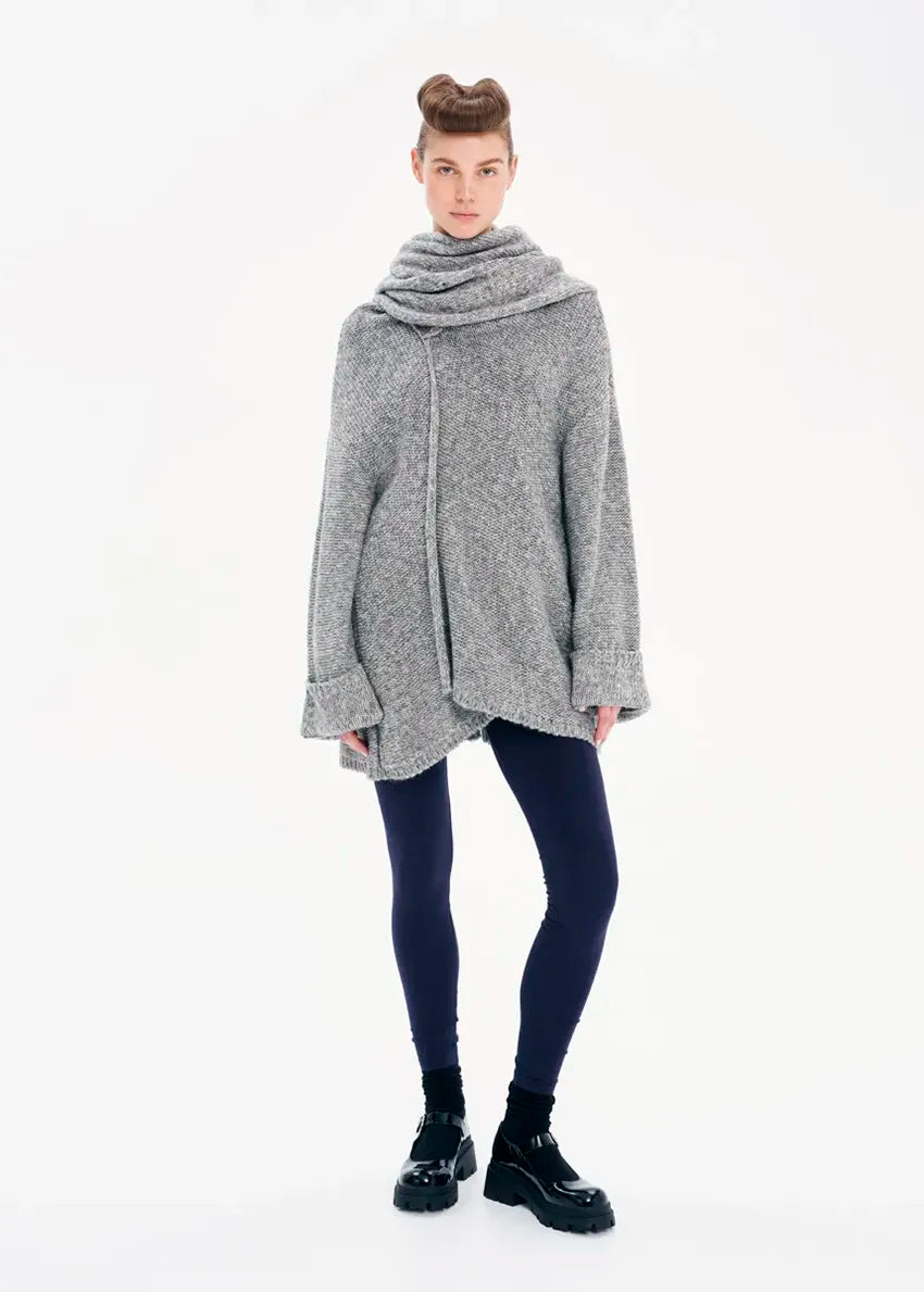 A model wearing a gray knit cardigan with long sleeves and a non-detachable scarf, paired with dark pants and black boots.