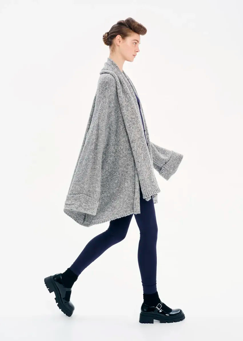 A model wearing a gray knit cardigan with long sleeves and a non-detachable scarf, paired with dark pants and black boots.