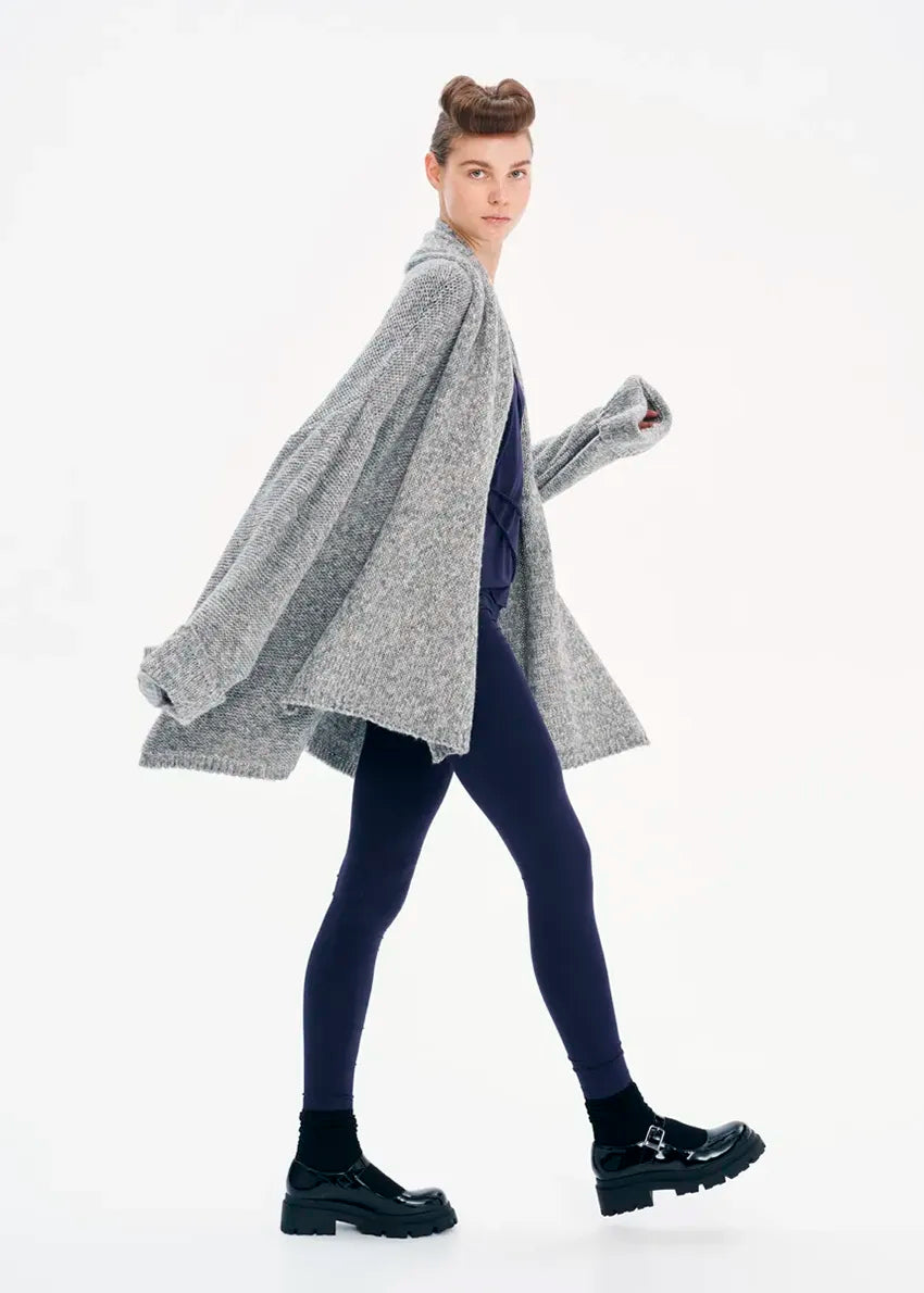 A model wearing a gray knit cardigan with long sleeves and a non-detachable scarf, paired with dark pants and black boots.