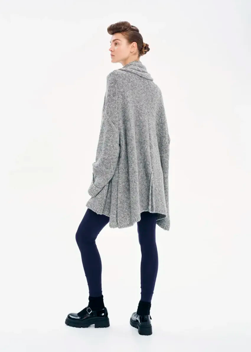 A model wearing a gray knit cardigan with long sleeves and a non-detachable scarf, paired with dark pants and black boots.