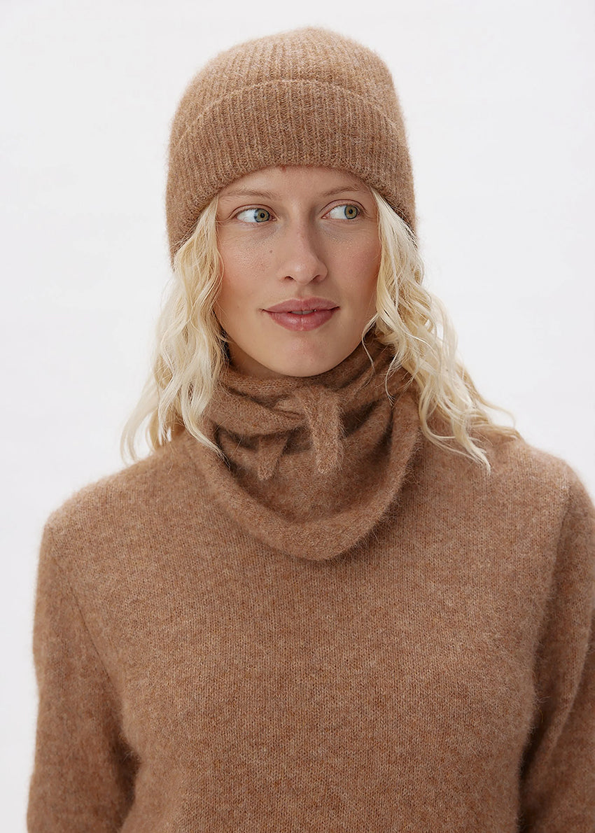 Woman wearing a brown knit hat and sweater against a white background