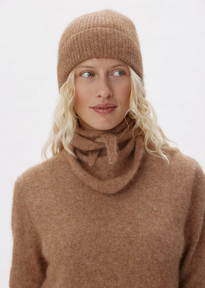 Woman wearing a brown knit hat and sweater against a white background