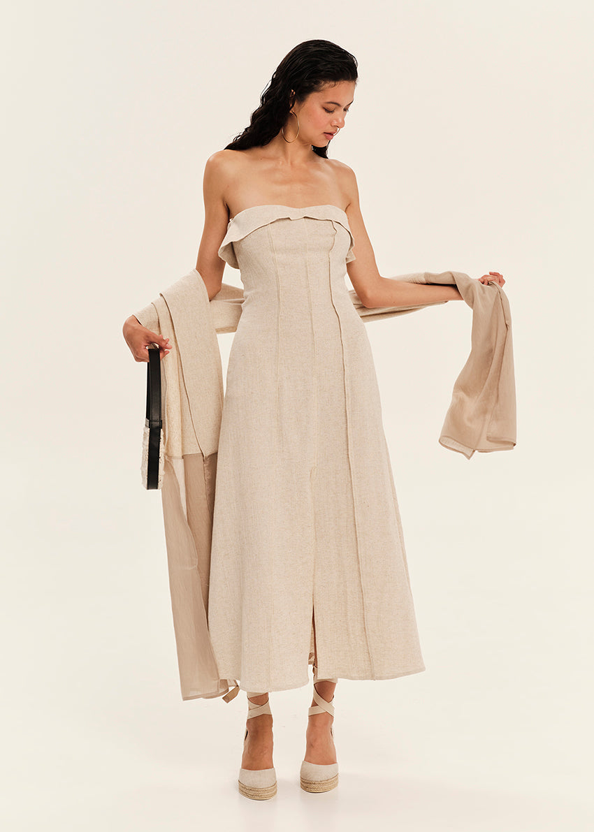 Woman wearing a beige strapless dress holding a matching scarf on a white background