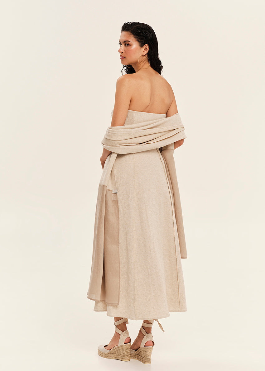 Woman wearing a beige strapless dress with a draped design on a plain background