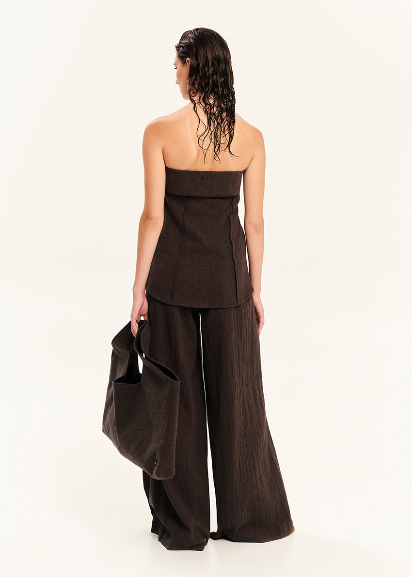 Woman wearing a black strapless top and wide-leg pants holding a matching bag on a white background