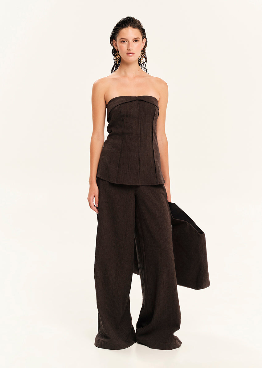 Woman wearing a black strapless top and wide-leg pants on a white background