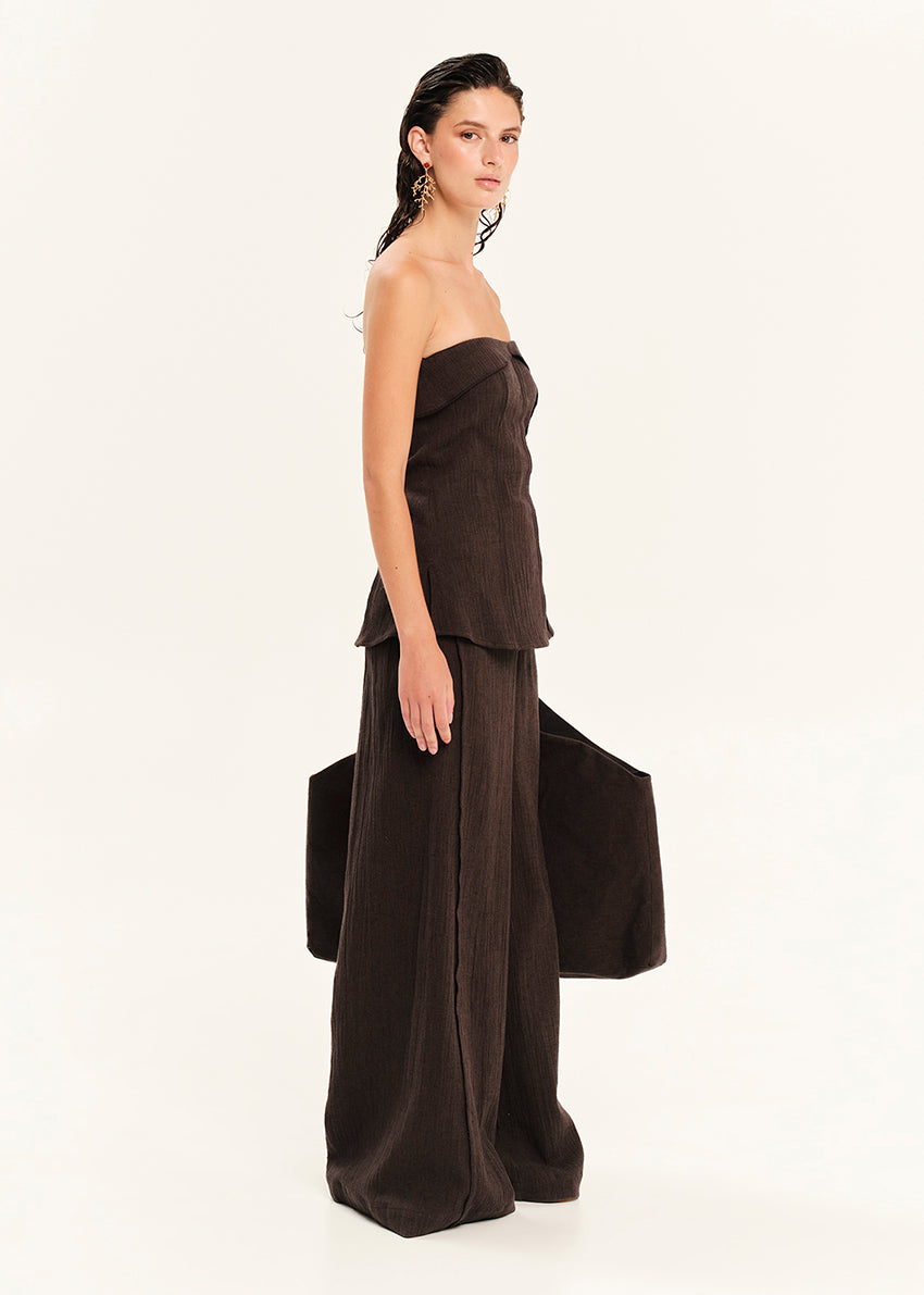 Woman wearing a dark brown strapless top and wide-leg pants on a white background