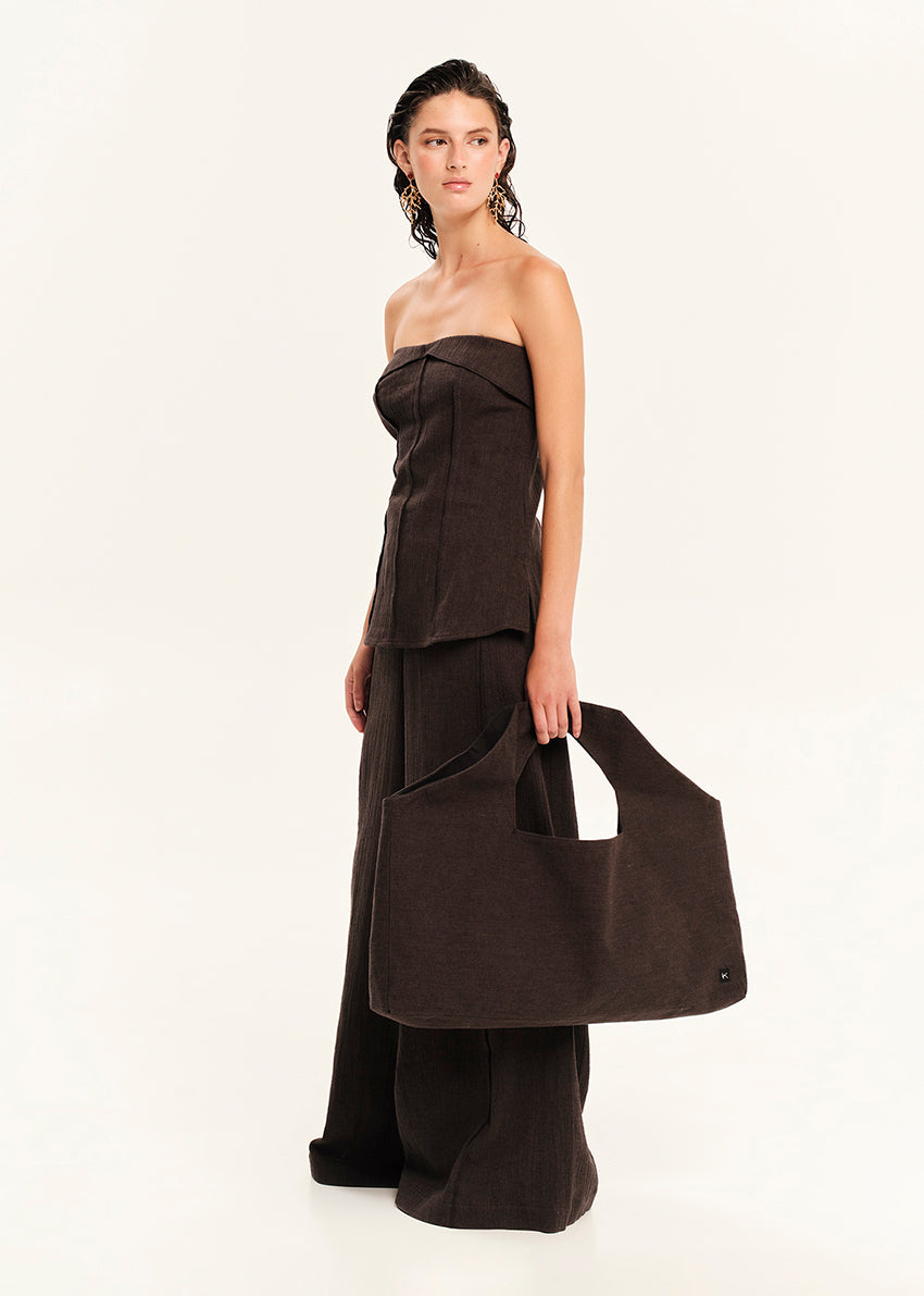 Woman wearing a black strapless top with matching pants holding a matching handbag on a white background